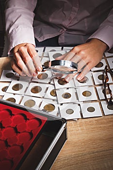 Collectible coin in the woman`s hand through the magnifying glass