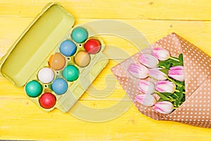 Collecting easter eggs. Colorful eggs and bouquet fresh tulip flowers on yellow background top view. Tradition celebrate