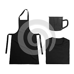 Collection of black objects isolated on white background. Black blank apron, black folded t-shirt, metal mug. Flat lay photo