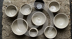 A collection of ceramic bowls displayed on a rough, textured stone surface. The bowls