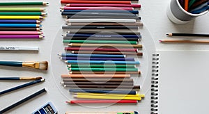 A collection of colored pencils is neatly arranged in parallel rows on a light-colored