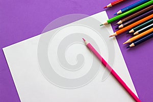 Collection of colored pencils on a purple background and white sheet of paper top view and copy space. Back to school