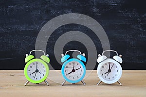 A collection of colorful alarm clocks over wooden desk in front of blackboard.