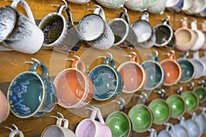 Collection of colorful ceramic mugs hanging on a wooden wall