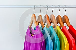 Collection of colorful rainbow t-shirts hanging on wooden clothes hanger in closet rack over white background