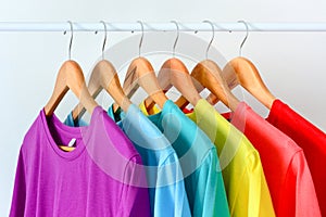 Collection of colorful rainbow t-shirts hanging on wooden clothes hanger on clothing rack over white background