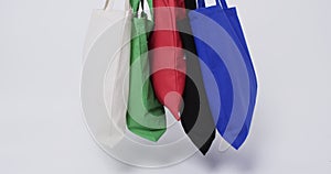 A collection of colorful tote bags in white, green, red, black, and blue hangs against a plain backg