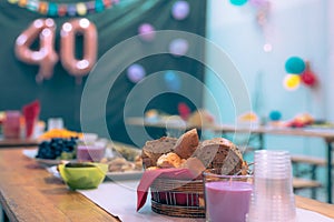 Collection of cookies and other food on a party table at a birthday event with visible baloons in the background. Focus on bread