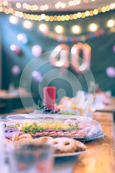 Collection of cookies and other food on a party table at a birthday event with visible baloons in the background. Focus on meat