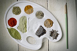 Collection of different spices on white plastic art palette, wooden background. Paint your food with spice.