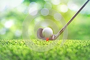 Collection of golf equipment resting on green grass. Blurred golf club and golf ball close up in grass field with sunset