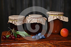 Collection of jars with homemade confitures with fresh ripe seasonal fruits and berries on a rustic wooden surface.