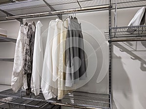 Collection of monotone colors tops and bottoms hanging inside an organized walk in closet with metal wire rack shelving