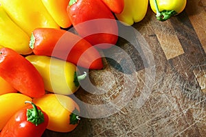 A collection of Red and Yellow Sweet Peppers Bordering Wood Cutting Board