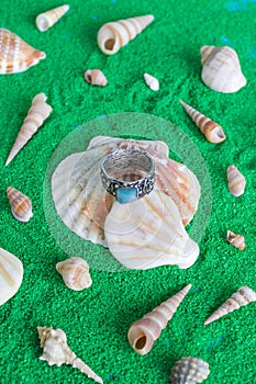 Collection of silver jewelries with blue stones on a background with artificial green sand and seashells.