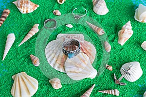 Collection of silver jewelries with blue stones on a background with artificial green sand and seashells.