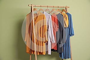 Collection of trendy women`s garments on rack near green wall. Clothing rental service