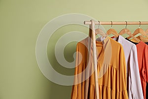 Collection of trendy women`s garments on rack near green wall, space for text. Clothing rental service