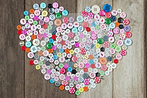 Collection of used buttons in heart shape on wood background.