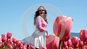 Collection of videos and photos where a girl in a white skirt walks through field with tulips blue background sky