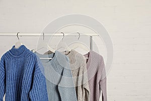 Collection of warm sweaters hanging on rack against white brick wall