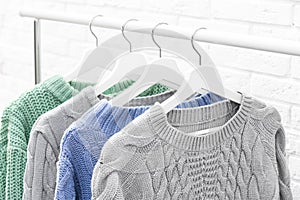 Collection of warm sweaters hanging on rack near wall, closeup