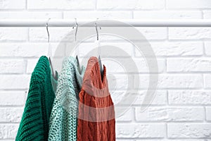 Collection of warm sweaters hanging on rack near wall, closeup. Space for text