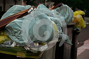 Collection of waste bins overfull with garbage. Plastic bags full of trash in bins. Organic waste in recycling bin photo