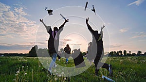 College graduates run to meet the sun and toss their caps and diplomas.