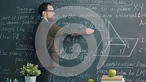 College professor giving maths lecture speaking and pointing at chalk board looking at camera