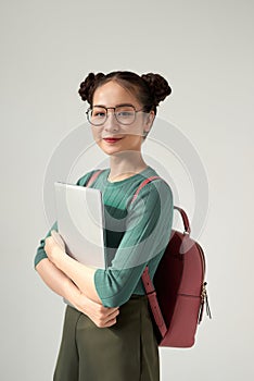 College student girl isolated on gray background, smiling at camera, pressing laptop to chest, wearing backpack, ready to go to