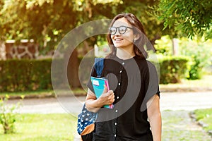 College student girl looking happy smiling outdoors. Student with book or notebook in campus park. Beautiful young woman in