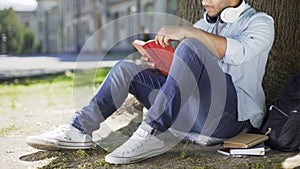 College student sitting under tree, taking book to read, literary studies, class