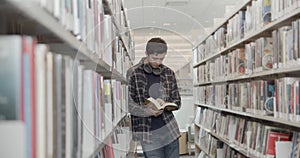 College student standing on floor in library, reading book. Midle shot