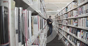 College student standing on floor in library, reading book. Vertical shape, side view, full length,