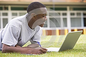 College student using laptop on campus lawn