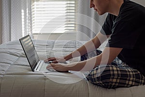 Student working on laptop computer on bed in morning light