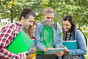 College students with bags and books using tablet PC in park