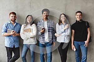 College students with books smiling to camera over grey wall