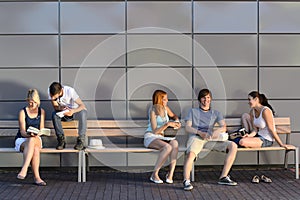 College students sitting on bench modern wall