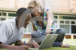 College students using laptop on campus lawn