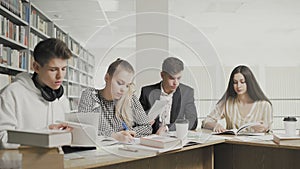 College students working together preparing for exams while sitting at table at university library