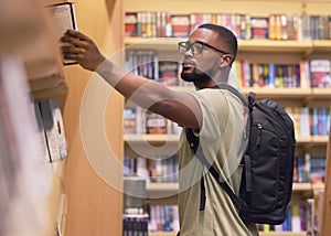 College or university student in a library taking a book from the shelf to read and study for education. Reading