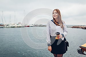 College woman student of Marine academy drinking coffee by sea wearing uniform. Girl walking in seaport of Odesa