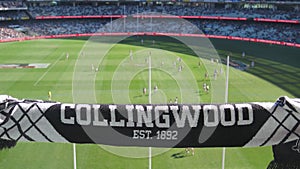 Collingwood Magpies supporter scarf with blurred background view of Melbourne Cricket Ground field during a footy game