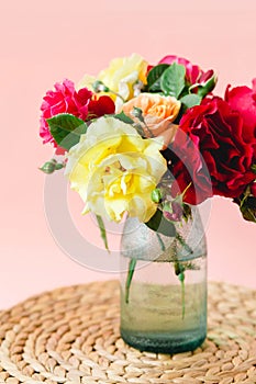 Coloful roses in vase on a wicker napkin on pink background