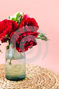 Coloful roses in vase on a wicker napkin on pink background