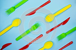 Colofulr plastic cutlery on light blue background. Pattern of green forks, yellow spoons and red knives