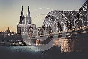 UNESCO Cathedral in Cologne Germany and Hohenzollern Bridge across Rhine River with Boat at Evening Sunset