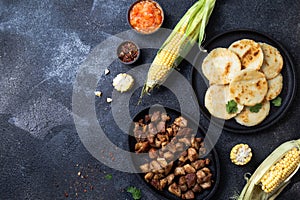 COLOMBIAN FOOD. Maize AREPAS and fried pork chicharron ans colombian tomato sauce. Top view. Black background